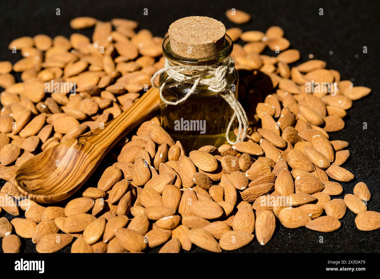 Mandel (Prunus dulcis, Prunus amygdalus, Amygdalus communis, Amygdalus dulcis), rohe Mandeln mit einer Glasflasche Mandelöl und einem Holzlöffel Stockfoto
