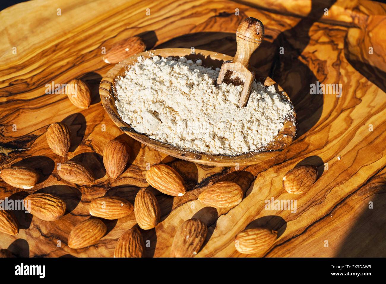 Mandel (Prunus dulcis, Prunus amygdalus, Amygdalus communis, Amygdalus dulcis), rohe und gemahlene Mandeln mit einer Holzschale und einem Holzlöffel Stockfoto
