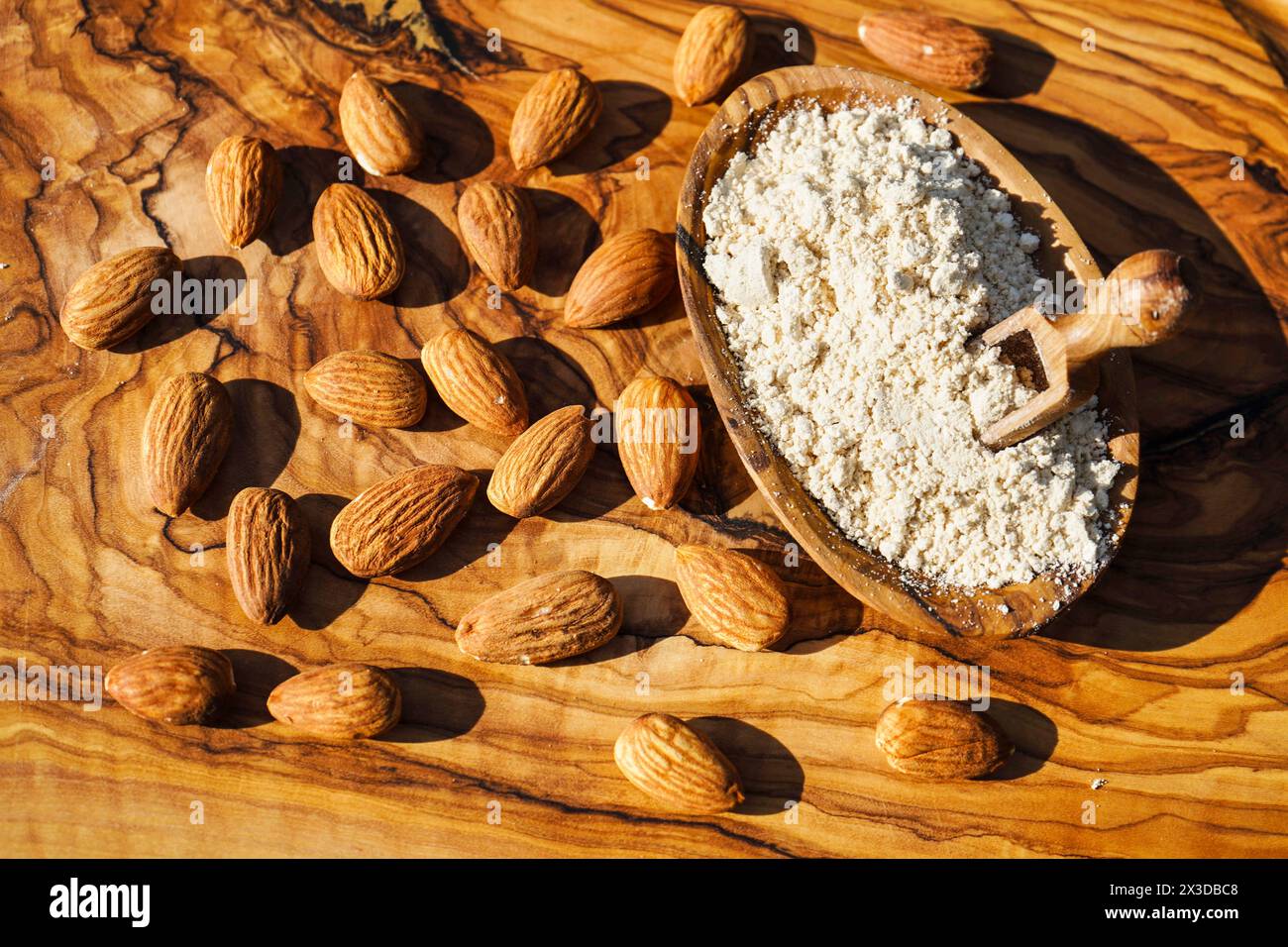 Mandel (Prunus dulcis, Prunus amygdalus, Amygdalus communis, Amygdalus dulcis), rohe und gemahlene Mandeln mit einer Holzschale und einem Holzlöffel Stockfoto