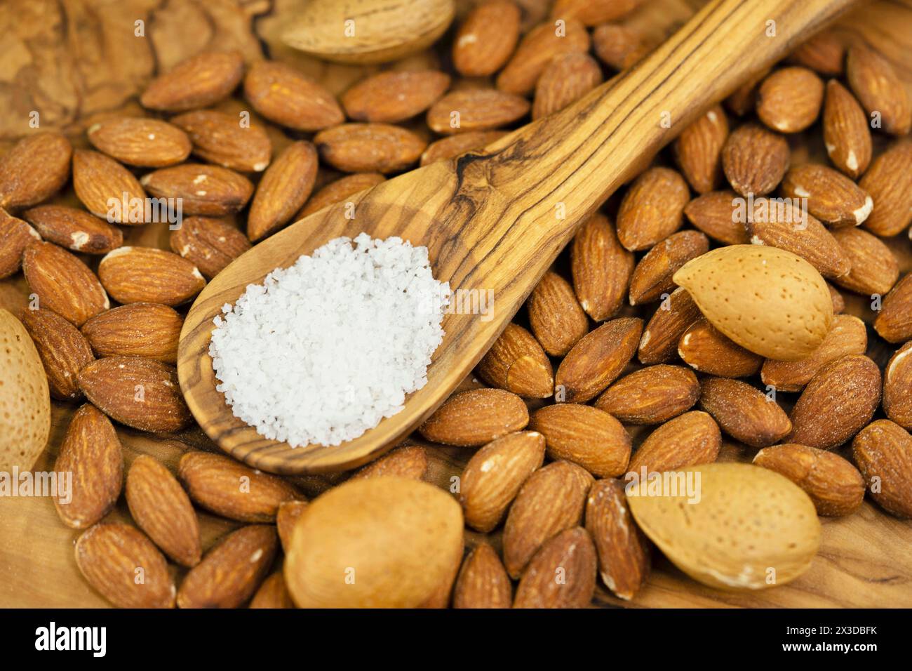 Mandel (Prunus dulcis, Prunus amygdalus, Amygdalus communis, Amygdalus dulcis), gesalzene Mandeln, ungesackte Mandeln und Holzlöffel mit Salz Stockfoto
