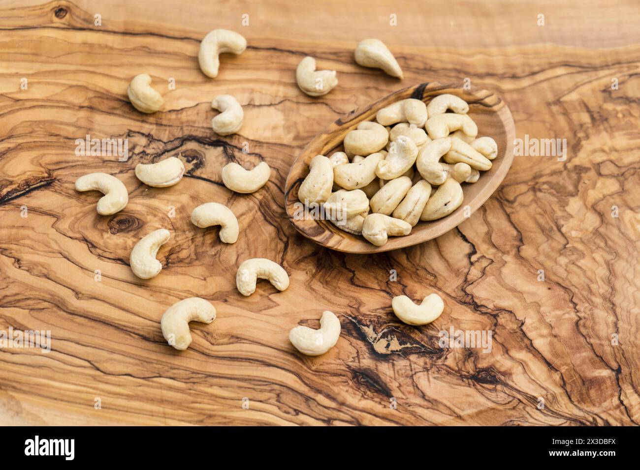 Cashewnüsse (Anacardium occidentale), Cashewnüsse in einer Holzschale auf einem Holztisch Stockfoto