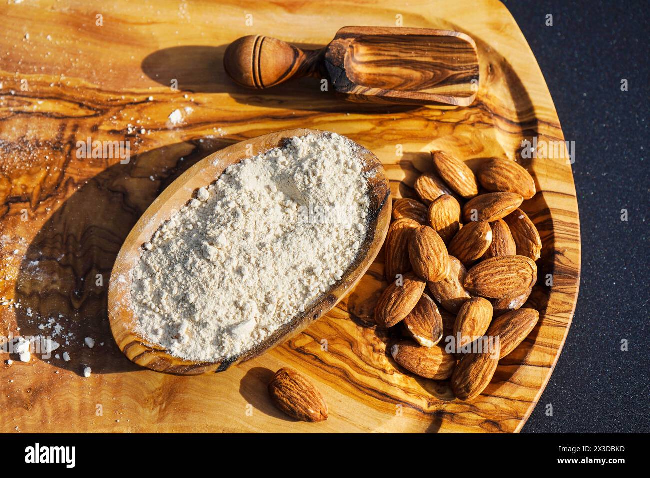 Mandel (Prunus dulcis, Prunus amygdalus, Amygdalus communis, Amygdalus dulcis), rohe und gemahlene Mandeln mit einer Holzschale und einem Holzlöffel Stockfoto