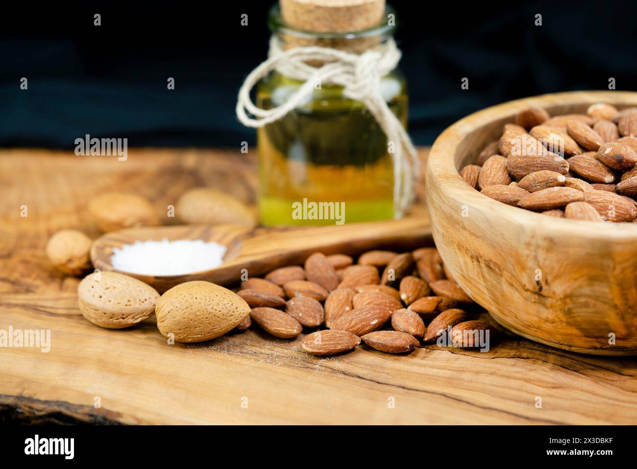 Mandel (Prunus dulcis, Prunus amygdalus, Amygdalus communis, Amygdalus dulcis), gesalzene Mandeln in einer Holzschale mit ungesackten Mandeln, Löffel mit sal Stockfoto