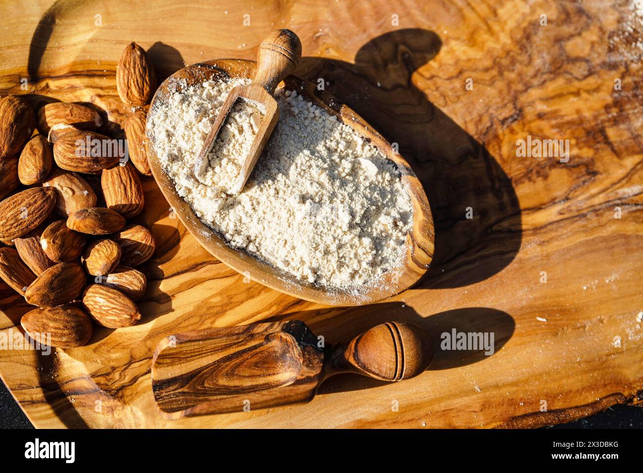 Mandel (Prunus dulcis, Prunus amygdalus, Amygdalus communis, Amygdalus dulcis), rohe und gemahlene Mandeln mit einer Holzschale und einem Holzlöffel Stockfoto