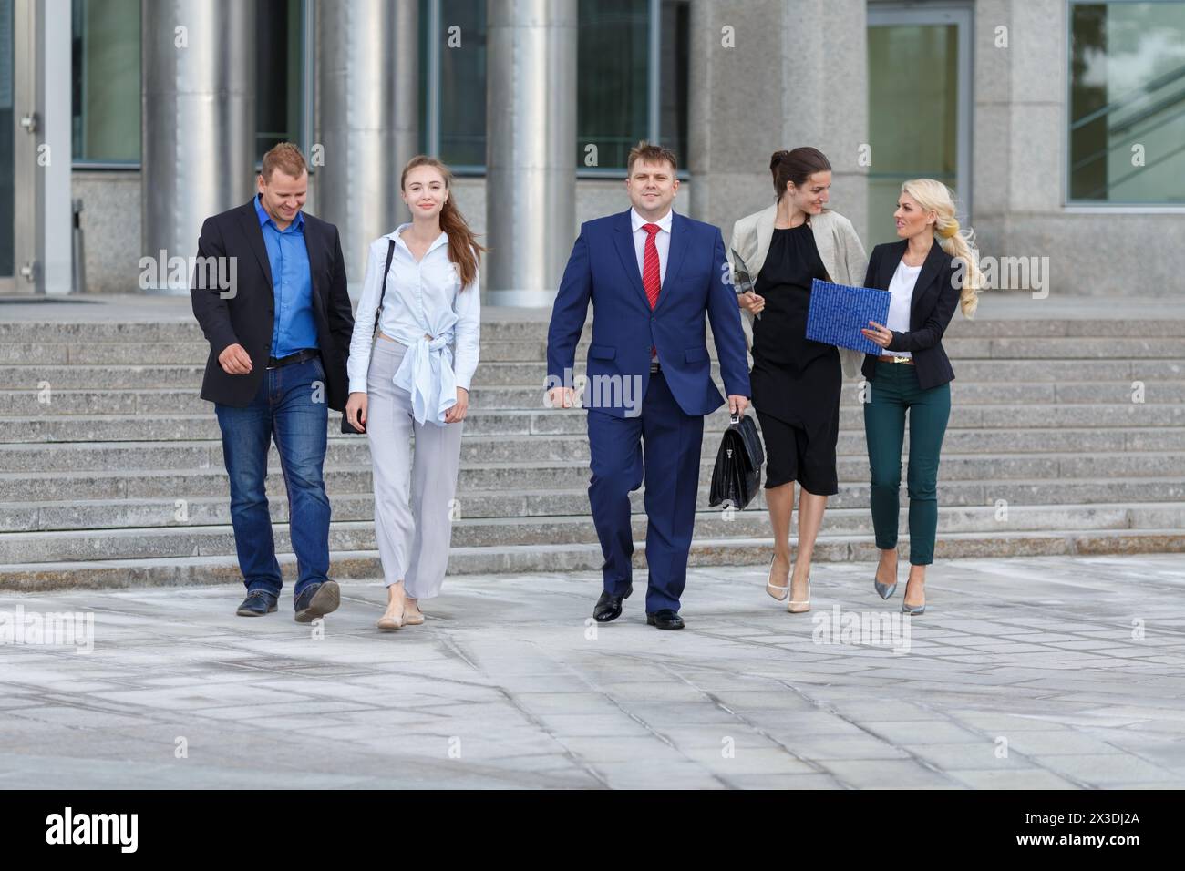 Fünf junge attraktive Geschäftsleute, die die Straße entlang laufen, vor dem Hintergrund von Geschäftszentren Stockfoto