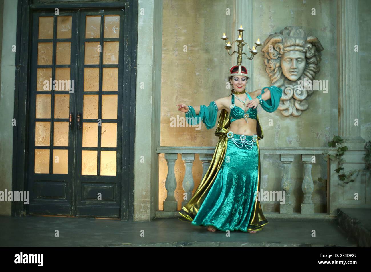 Eine schöne Frau in einem grünen Kleid, dekoriert mit Perlen und Kronleuchter auf dem Kopf, spielt arabischen Tanz Stockfoto