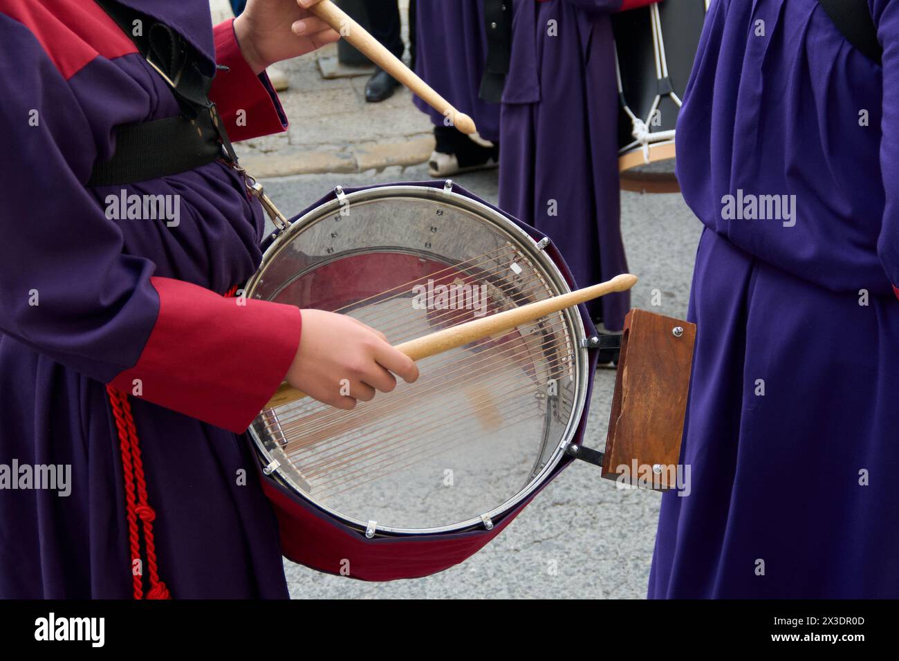 Musiker, die während einer Prozession Trommeln spielen. Sie sind in farbenfrohe Gewänder gekleidet, die eine lebendige und rhythmische Atmosphäre schaffen, die zur Reflexion einlädt Stockfoto