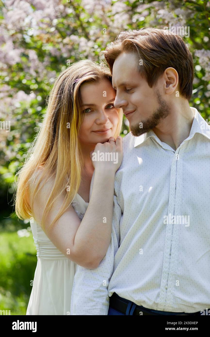 Die junge Frau steht mit dem Kinn und der Hand auf der Schulter eines jungen bärtigen Mannes im grünen Park Stockfoto