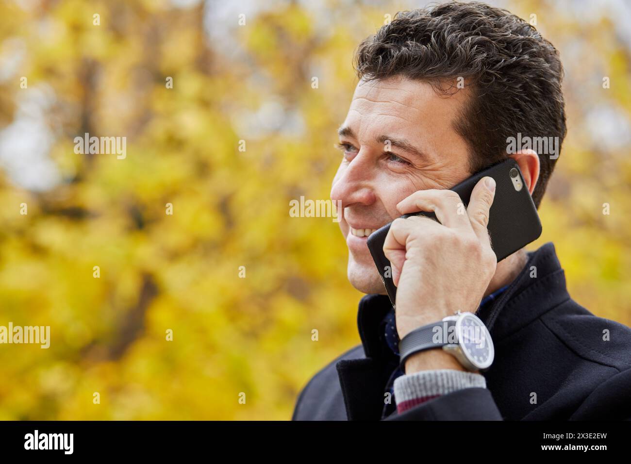 Lächelnder Mann im Mittelalter, der draußen im Park telefoniert. Stockfoto