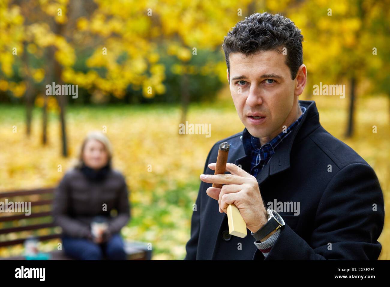 Der Mann raucht Zigarren und woamn auf der Bank im Herbstpark. Stockfoto