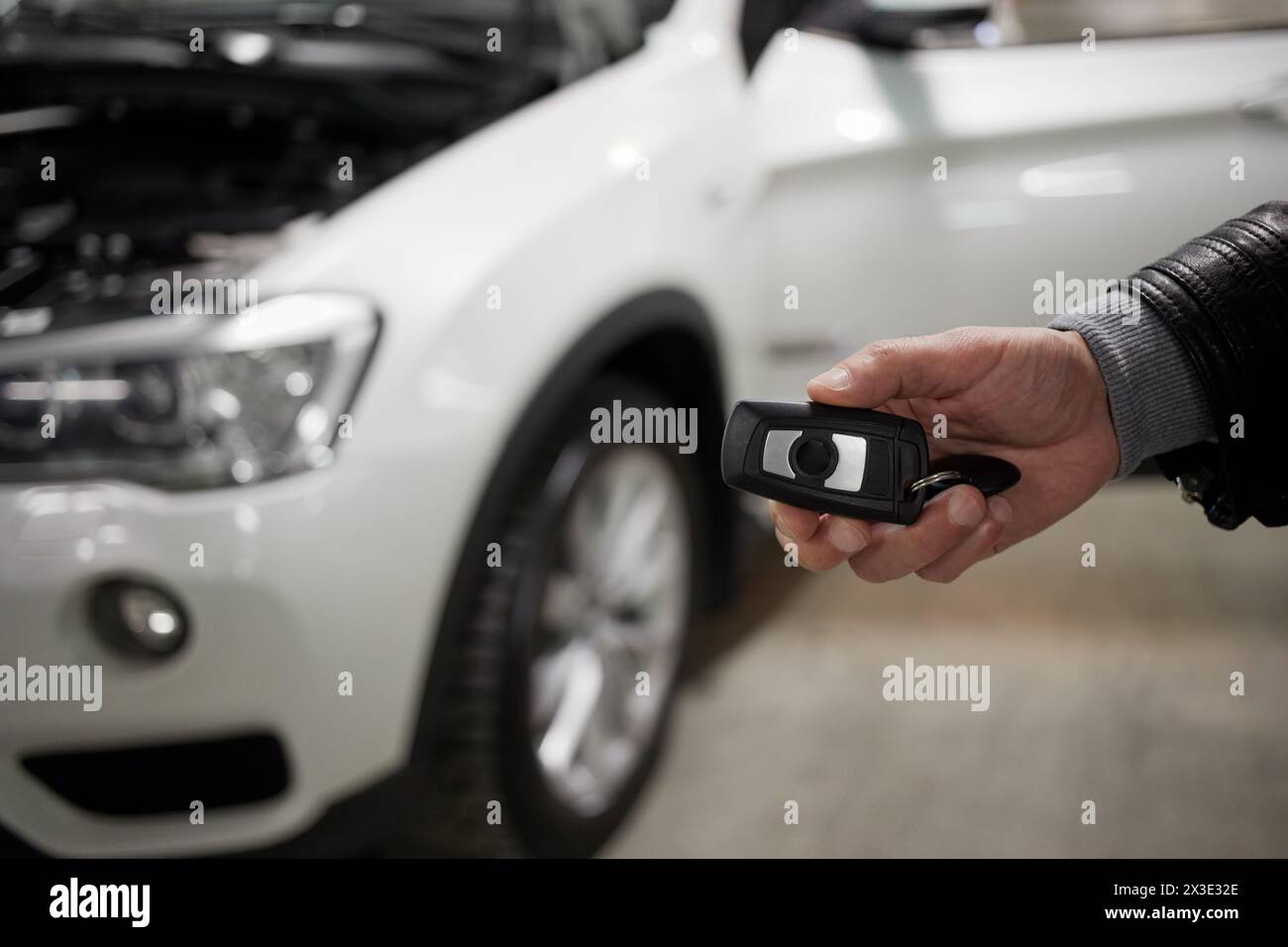 Männliche Hand, die den Autoschlüssel gegen das weiße Auto hält. Stockfoto