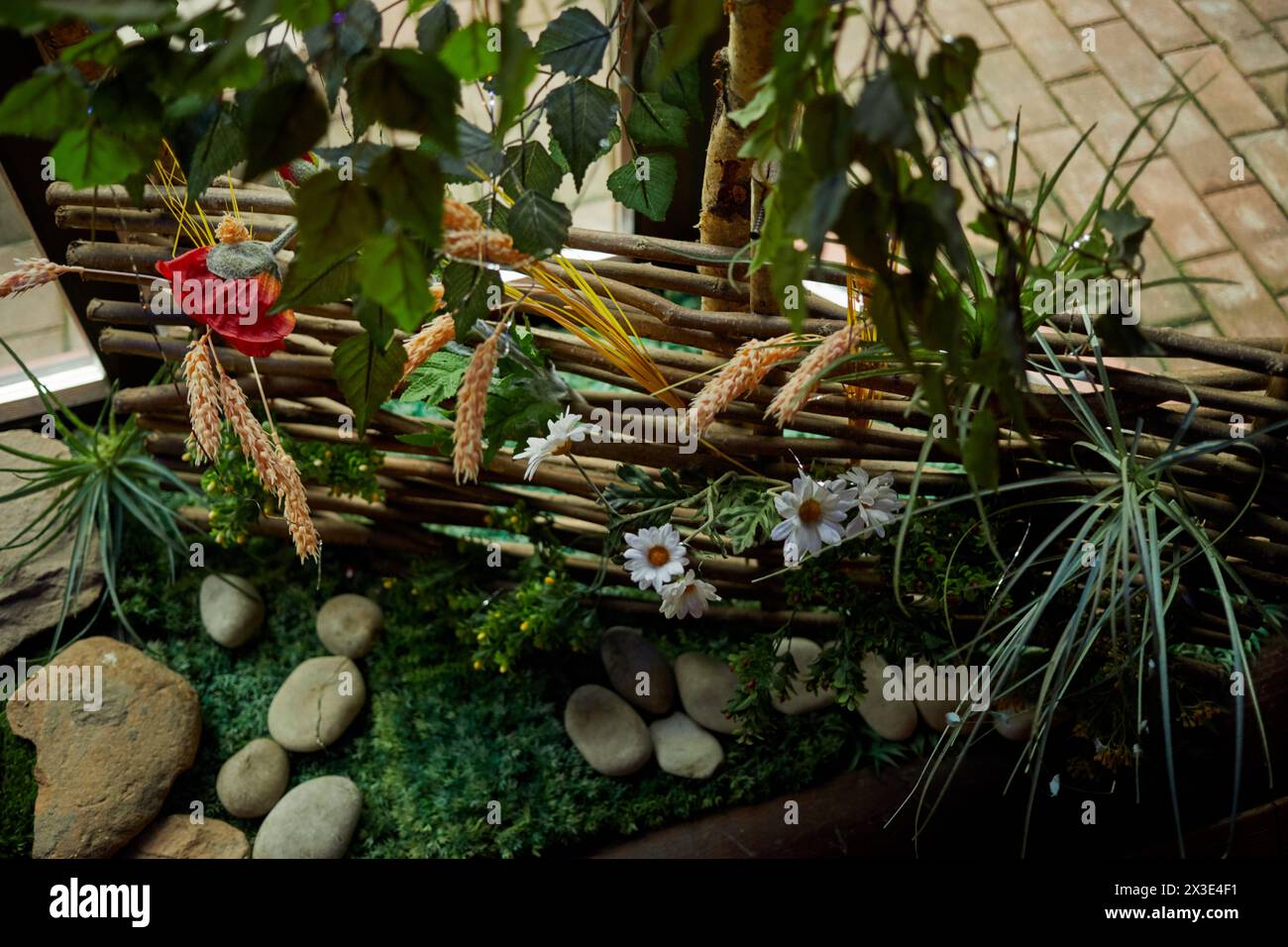 Dekorativer Korbzaun mit künstlichen Bäumen, Blumen, Gras. Stockfoto