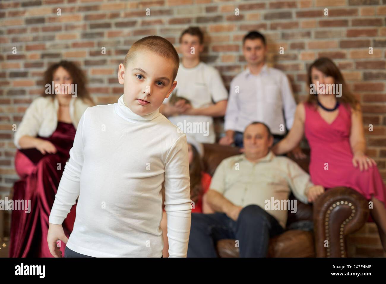 Porträt von Jungen gegen Familie, die auf Sofa im Zimmer sitzt. Stockfoto