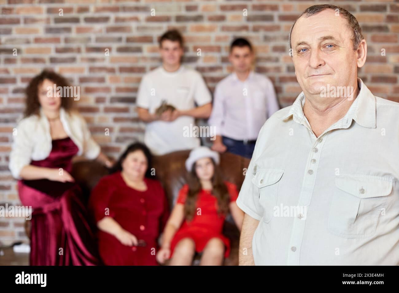 Porträt eines älteren Mannes gegen Familie, die auf dem Sofa im Zimmer sitzt. Stockfoto