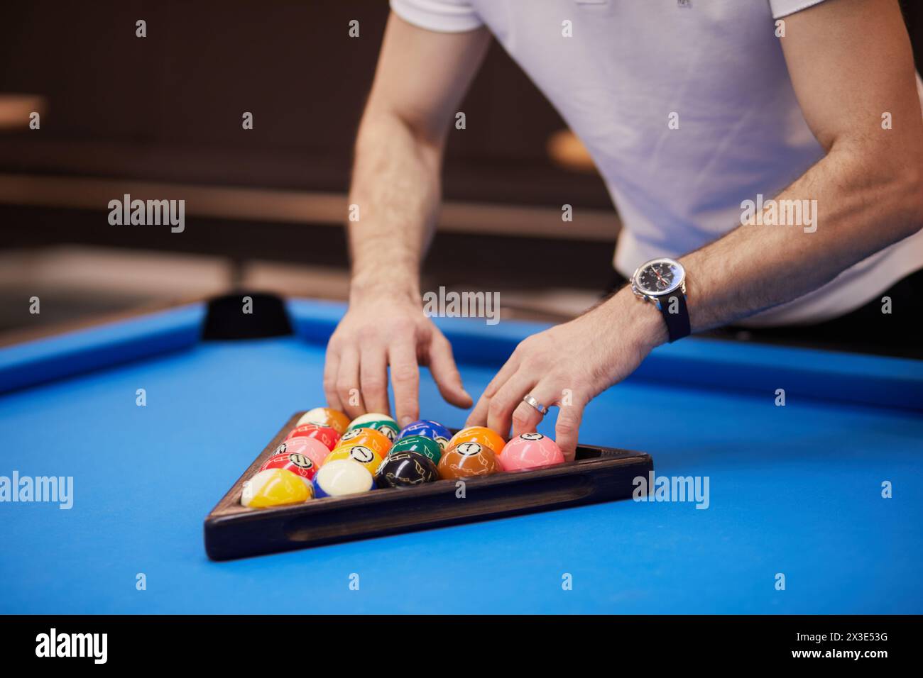 Der Mann bereitet Bälle auf einem blauen Billardtisch vor und richtet sie in einem Dreiecksregal aus. Stockfoto