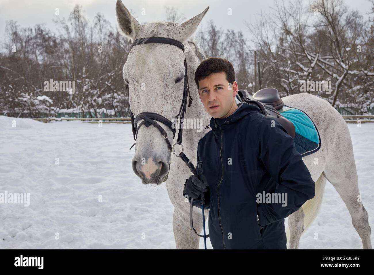 Mann steht im Park mit weißem Pferd am Wintertag. Stockfoto