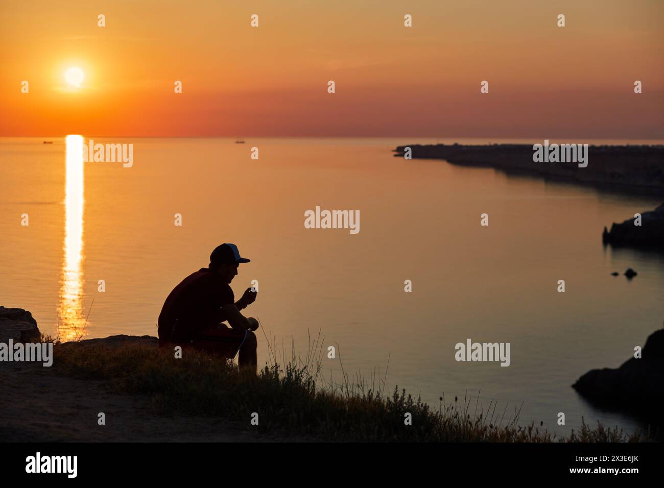 Der Mann sitzt am Meer bei Sonnenuntergang im Sommer. Stockfoto