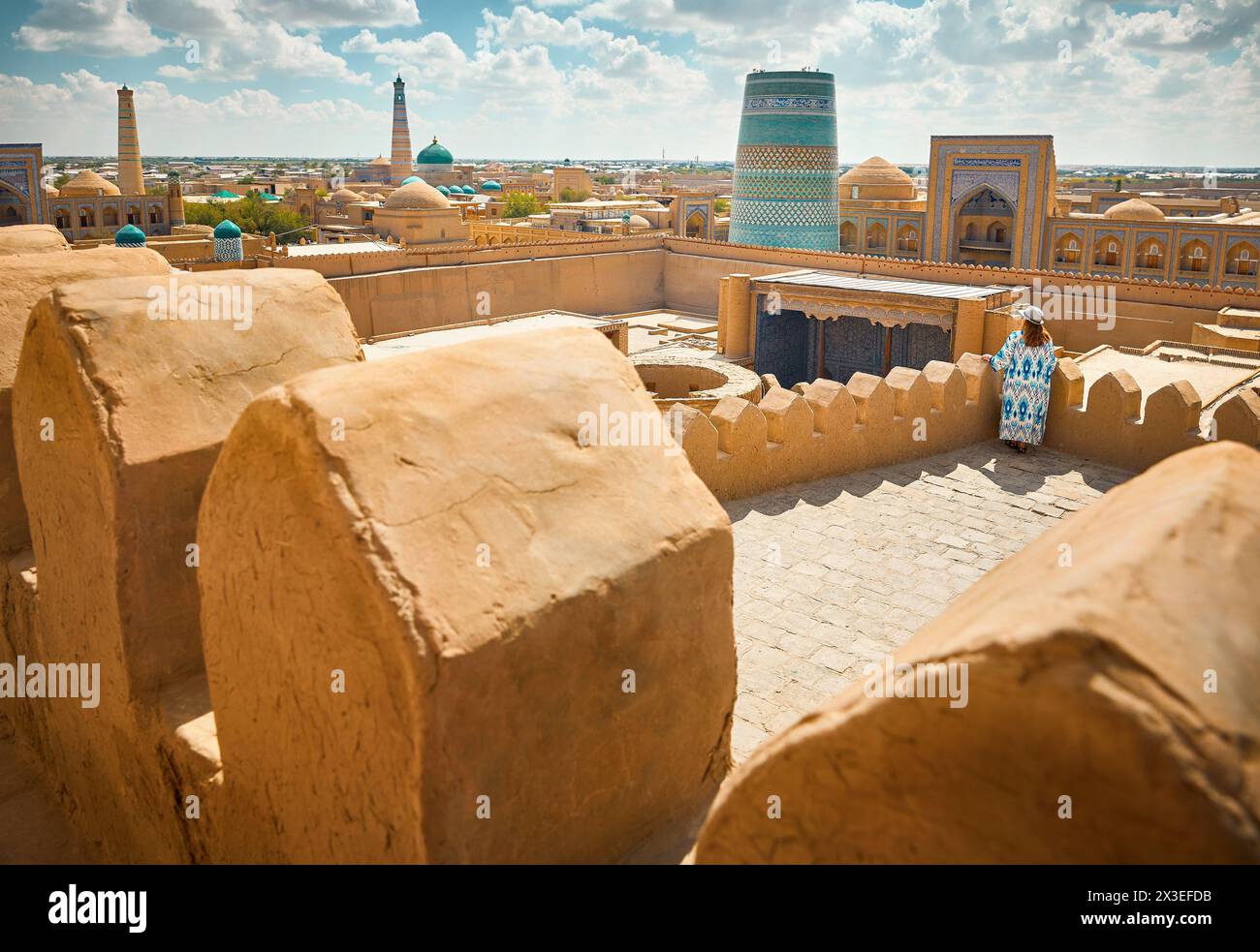 Junge Frau in ethnischer Kleidung mit blauem Ornament, die auf dem Dach der Festung Stadtmauer in Itchan Kala der alten Stadt Chiwa in Usbekistan läuft. Stockfoto