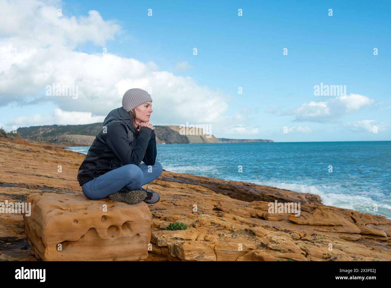 Frau, die auf einem Felsen sitzt und die Wellen beobachtet, trauriges, einsames Konzept Stockfoto