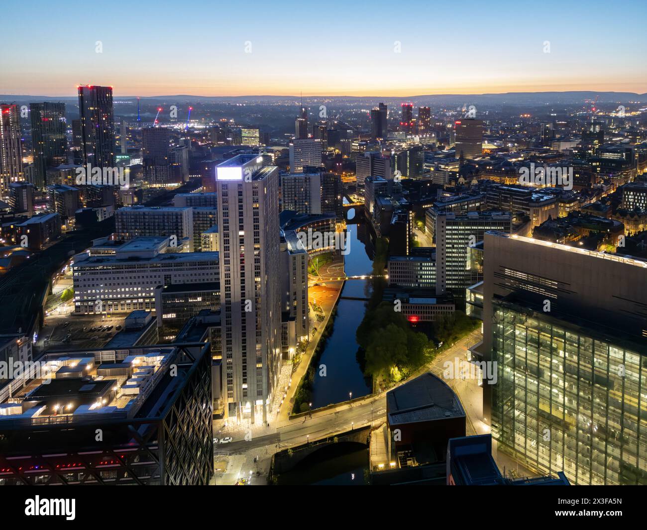 Atemberaubender Blick aus der Vogelperspektive auf die Stadt am Fluss mit glitzernden Lichtern, die während der Dämmerung vom Wasser reflektiert werden Stockfoto