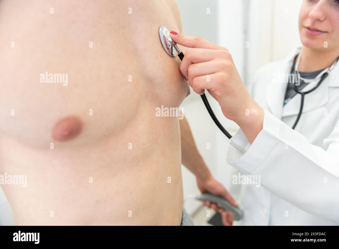 Ein lächelnder Arzt benutzt ein Stethoskop, um einem Patienten Brust in einer medizinischen Klinik zuzuhören. Stockfoto