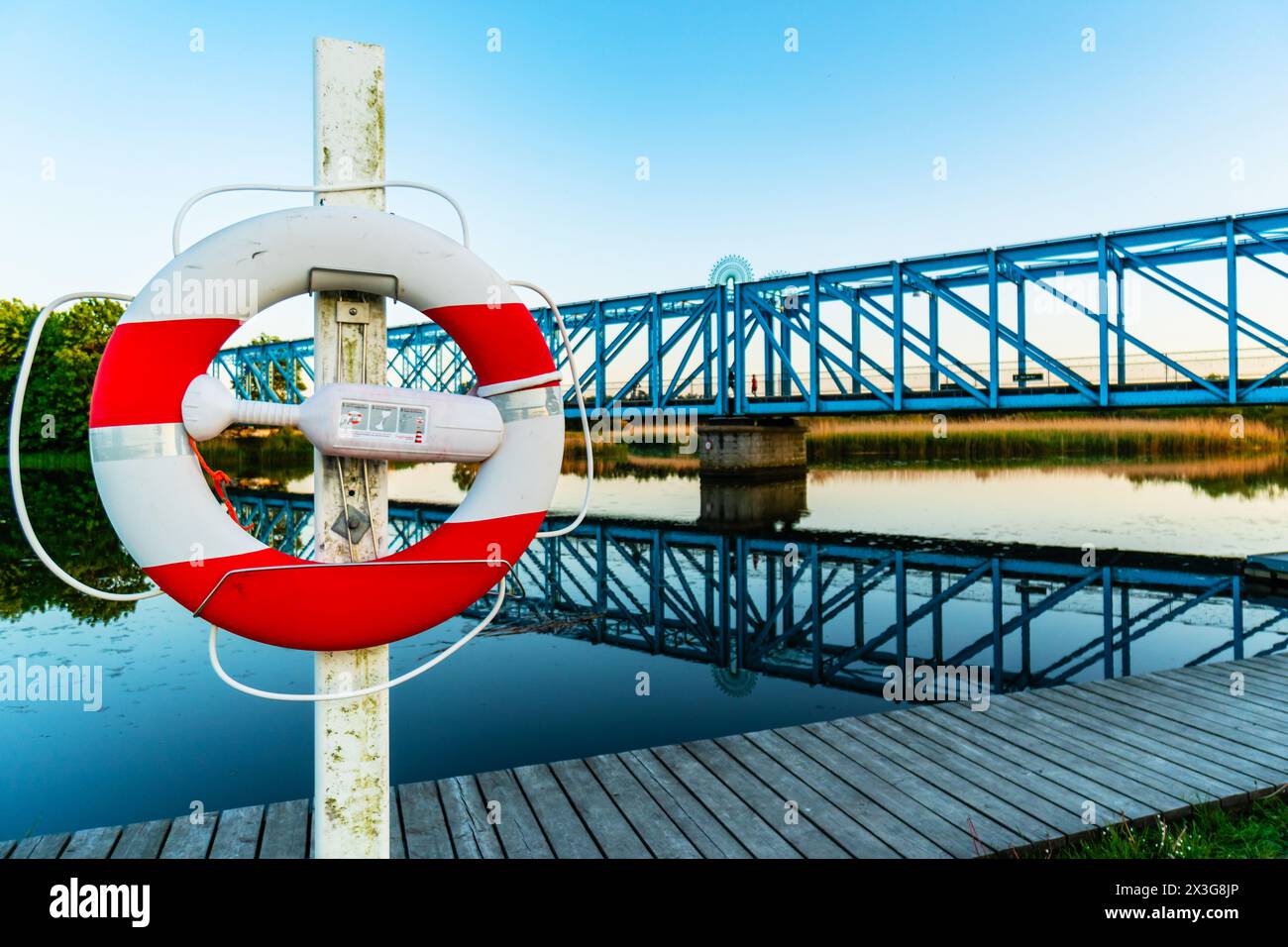 Lebensretter auf einem hölzernen Dock in der Nähe der Eisenbahnbrücke über einen Fluss in einem Wildtier-Sumpfgebiet zur blauen und goldenen Stunde mit Wasserreflektionen Stockfoto