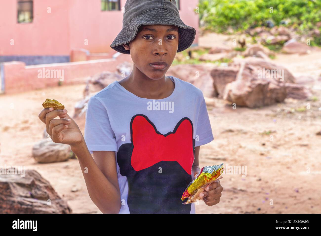 afrikanisches Mädchen im Dorf, das draußen im Hof Snacks isst Stockfoto