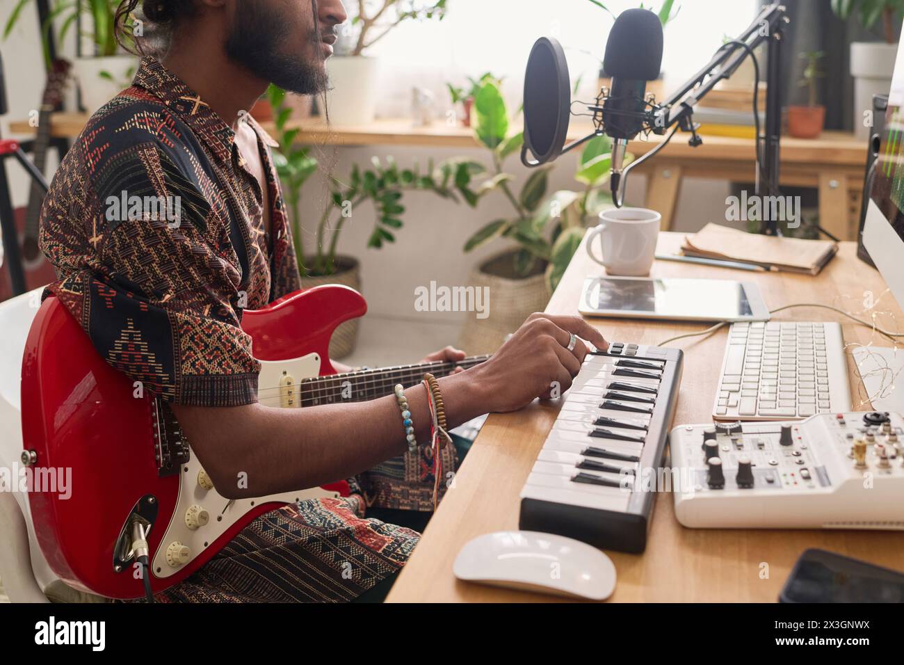 Zugeschnittene Aufnahme eines jungen kreativen männlichen Komponisten mit E-Gitarre und elektronischem Synthesizer, der neue Musik kreiert und aufnimmt Stockfoto