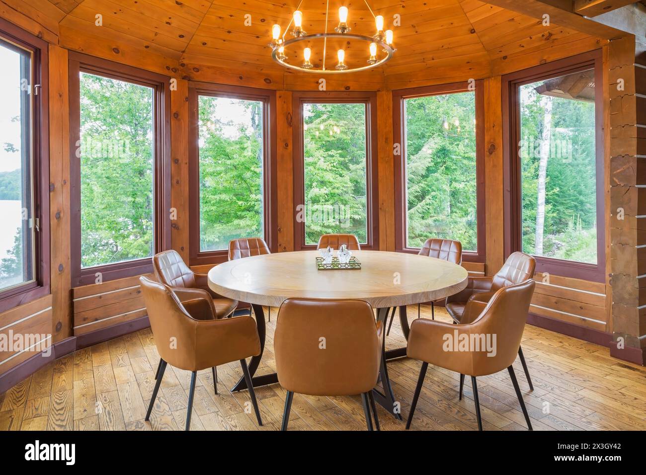 Runder hölzerner Esstisch mit braunen Ledersesseln im Esszimmer in einem gefrästen östlichen weißen Kiefernholz und flachem Holzprofil Haus, Quebec Stockfoto