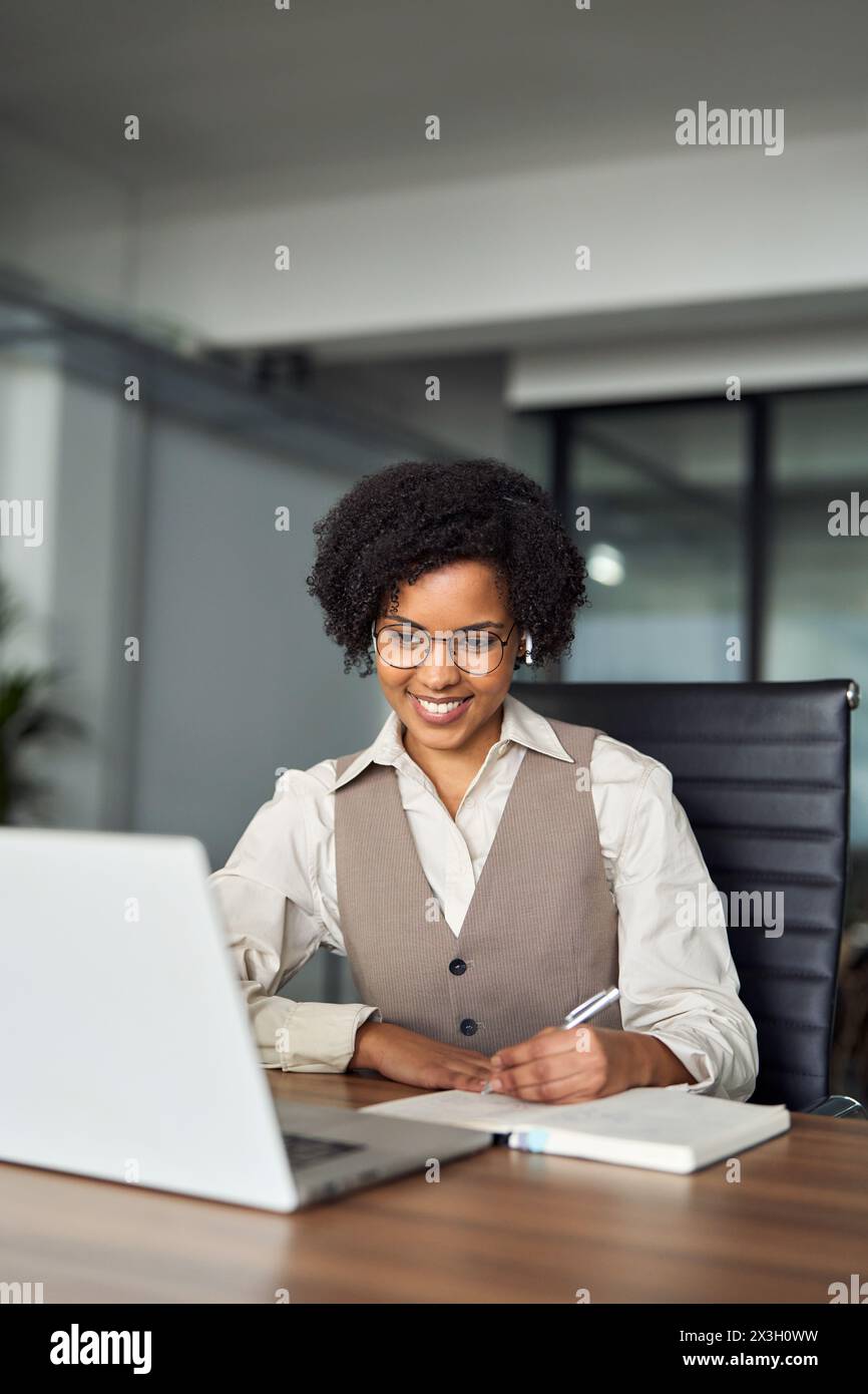 Glückliche junge afrikanische Geschäftsfrau mit Ohrstöpseln, die ein Hybrid-Büro-Meeting hat. Stockfoto