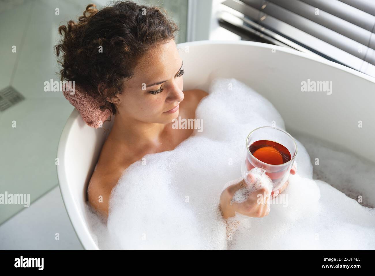 Eine junge kaukasische Frau, die sich zu Hause im Sprudelbad entspannt und Tee hält Stockfoto