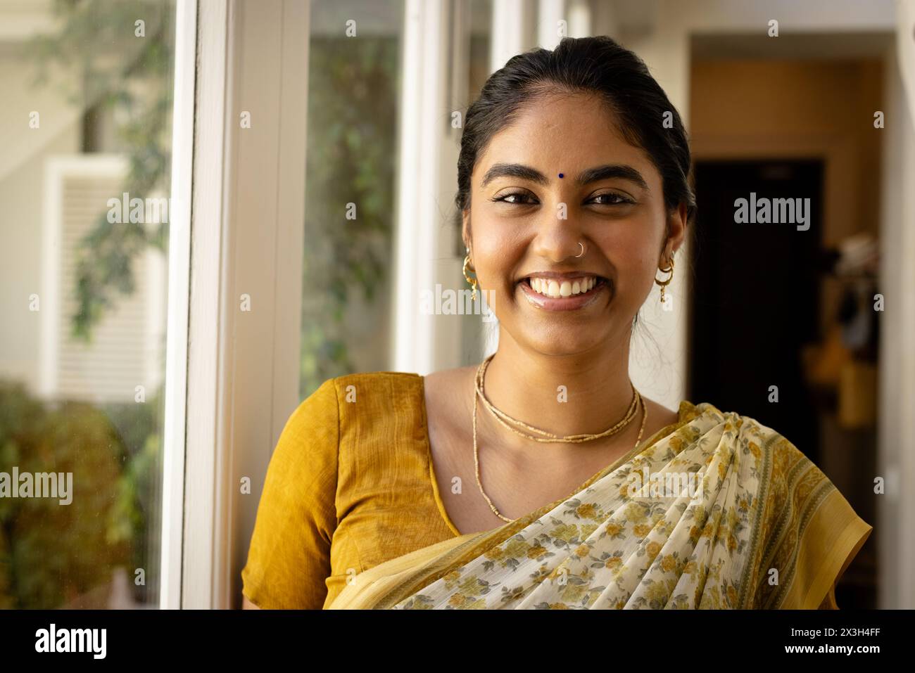 Eine junge indische Frau trägt traditionellen gelben Saree und lächelt zu Hause Stockfoto