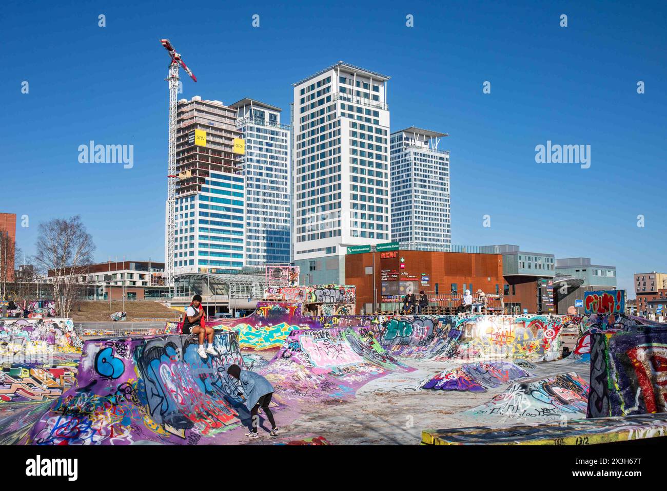 Graffiti bedeckten Suvilahti DIY Skatepark, Redi Mall und Kalasatama Hochhäuser vor klarem blauem Himmel in Helsinki, Finnland Stockfoto