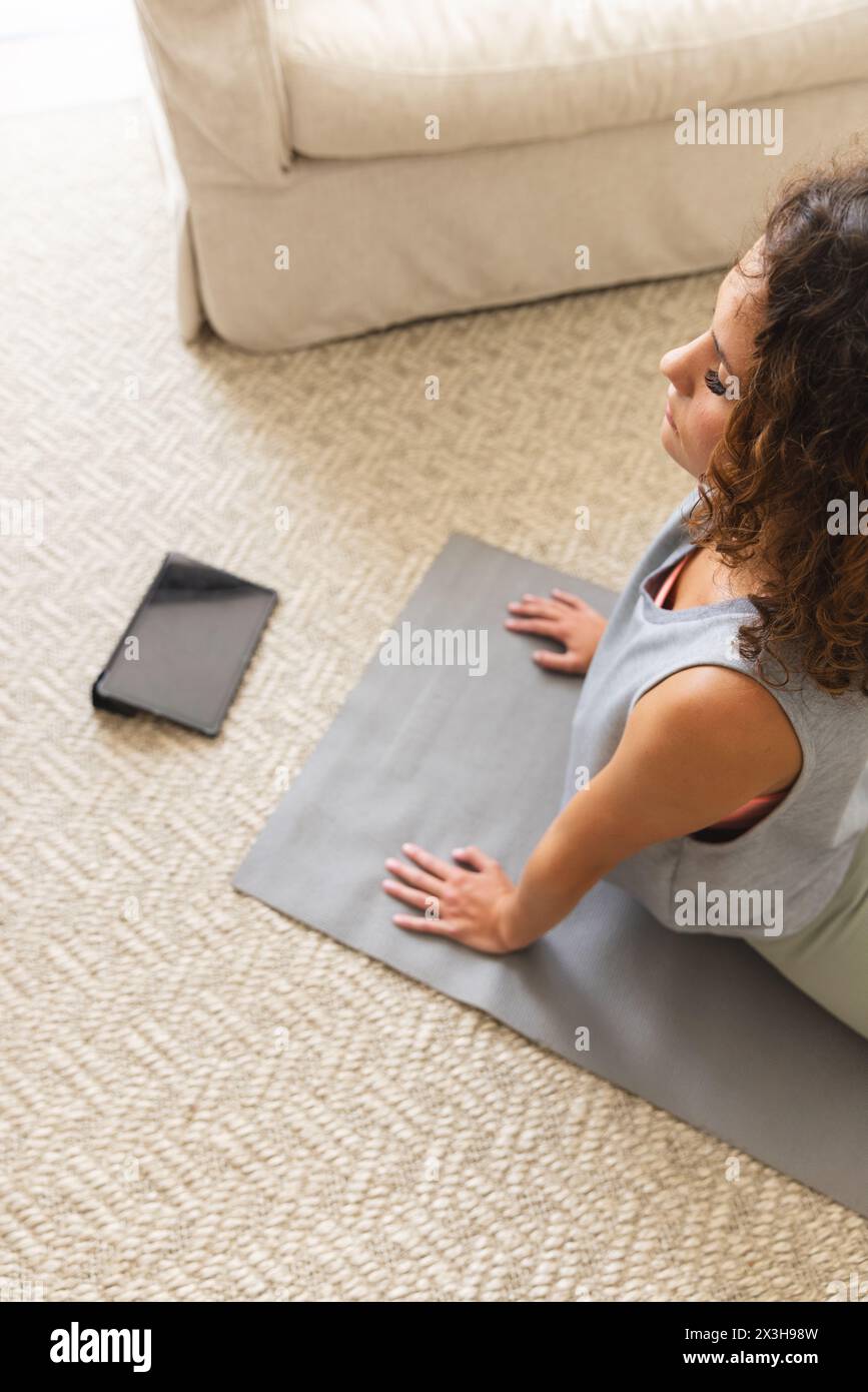 Eine junge kaukasische Frau mit lockigen Haaren, die zu Hause Yoga praktiziert, Kopierraum Stockfoto