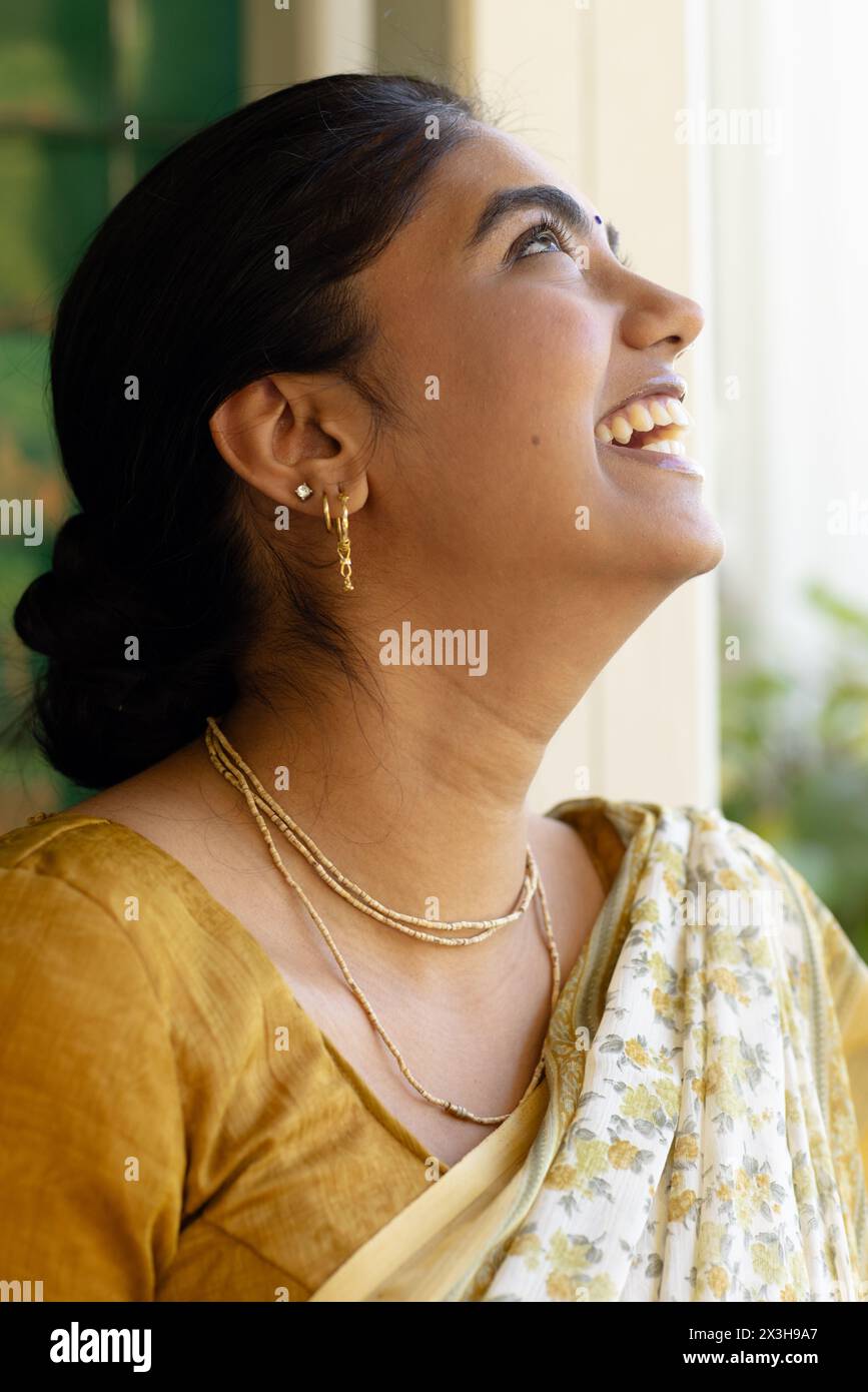 Indische junge Frau, die traditionellen Saree trägt und zu Hause mit einem Lächeln aufblickt Stockfoto