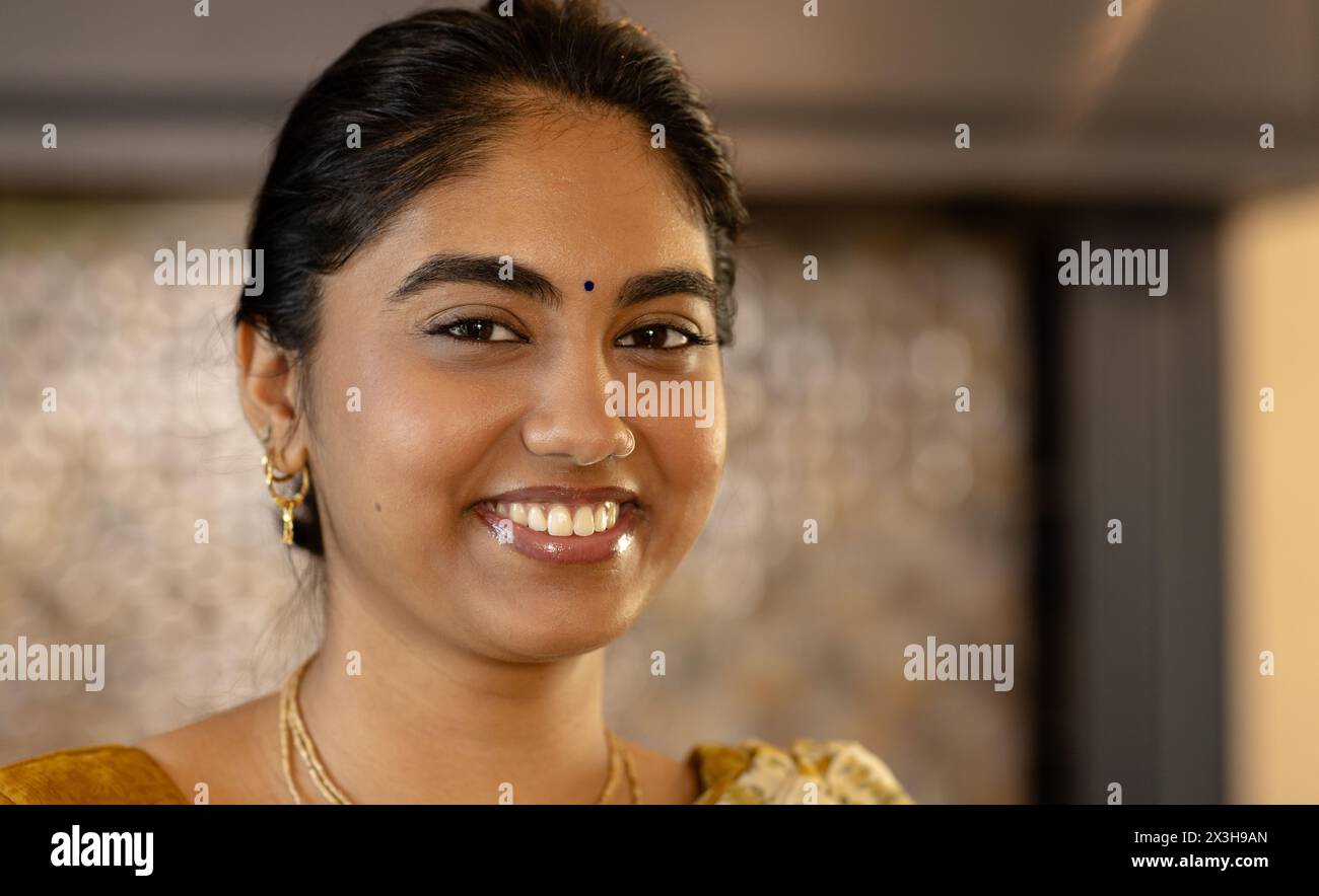 Die junge indische Frau trägt goldene Ohrringe und lächelt zu Hause in die Kamera Stockfoto
