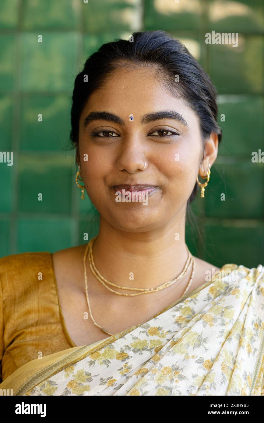 Indische junge Frau mit traditionellem Saree, die zu Hause sanft lächelt Stockfoto