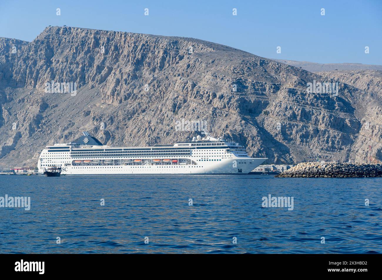 Khasab, Oman - 1. Januar 2024: Ein majestätisches weißes Kreuzfahrtschiff legt in der Nähe der zerklüfteten Berge an und bietet eine harmonische Mischung aus natürlicher Schönheit und Huma Stockfoto