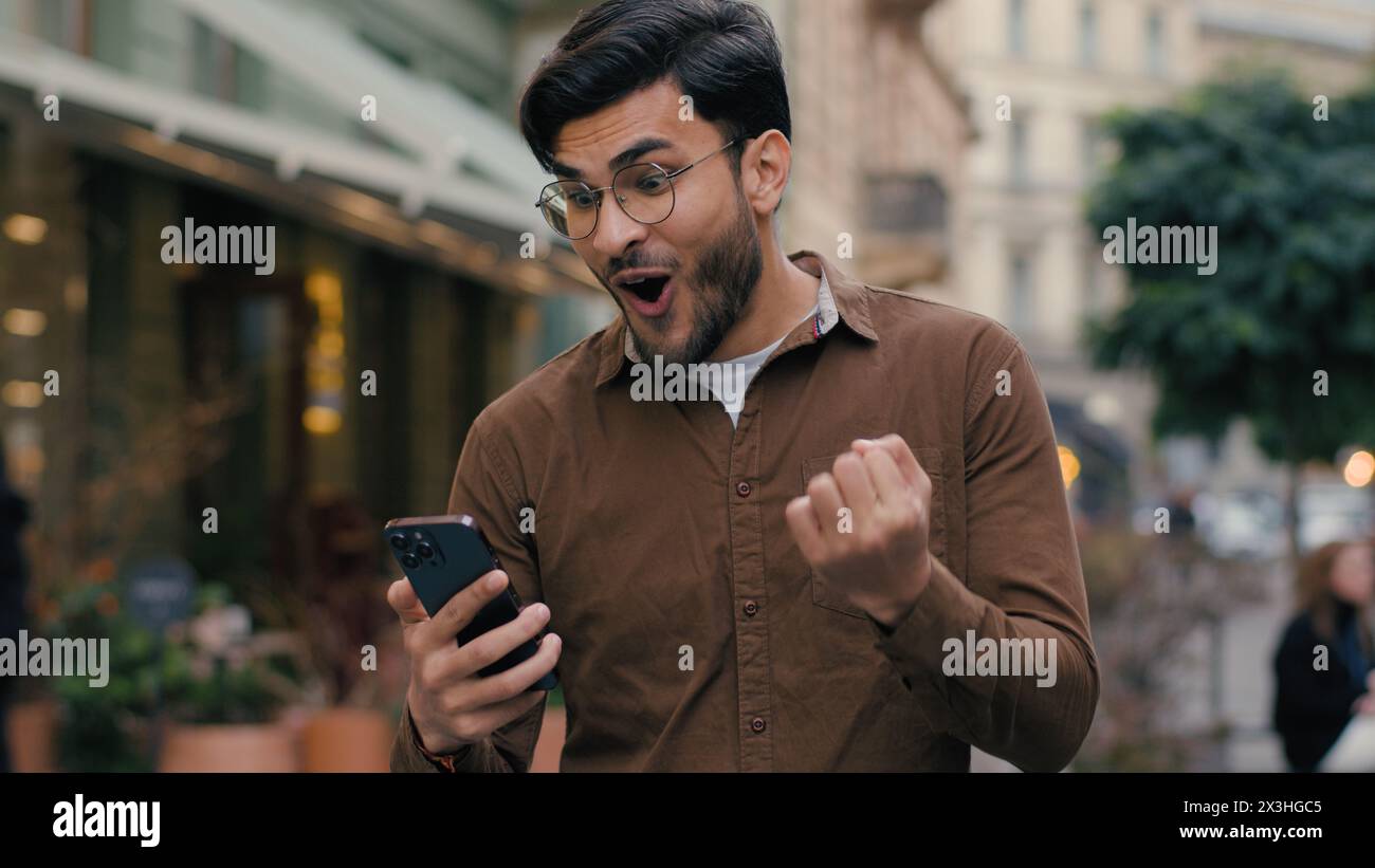 Glücklicher hoffnungsvoller indischer arabischer ethnischer Mann Mann Geschäftsmann männlicher junger Student hält Handy-Smartphone und wünscht Hoffnung betend gekreuzt Stockfoto