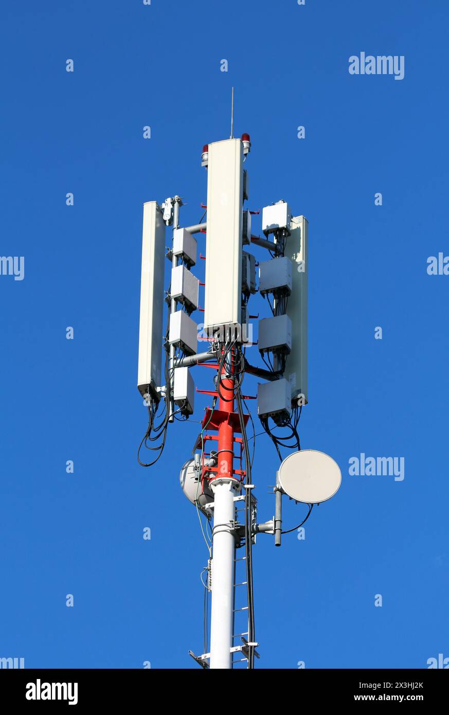 Mobiltelefonsender und -Antennen in verschiedenen Formen und Größen, die auf einem hohen starken roten und weißen Metallmast auf klarem blauem Hintergrund montiert sind Stockfoto