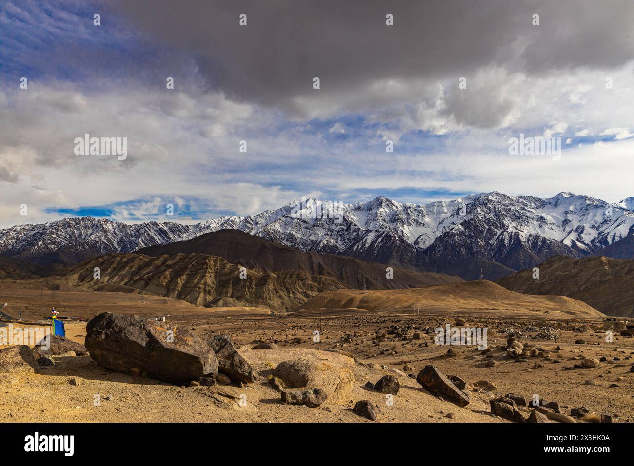 Eine Panoramalandschaft mit Felsen im Vordergrund, schneebedeckten Bergen in der Mitte und dunklen Wolken am Himmel Stockfoto