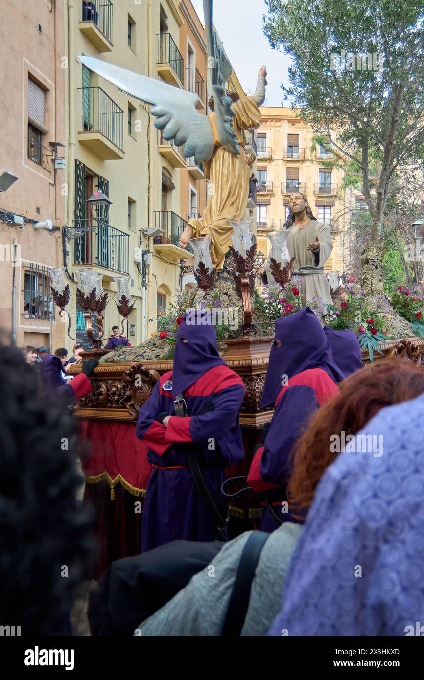 Tarragona, Spanien - 27. April 2024: Karwochenprozession mit Engelsstatue und Pönitenten auf einer historischen Straße. Stockfoto