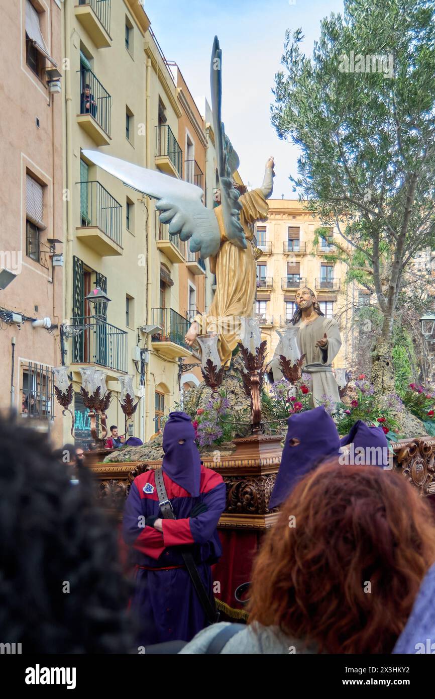 Tarragona, Spanien - 27. April 2024: Bild der Karwoche mit einer goldenen Engelstatue und Bußleuten auf einer historischen Straße. Stockfoto