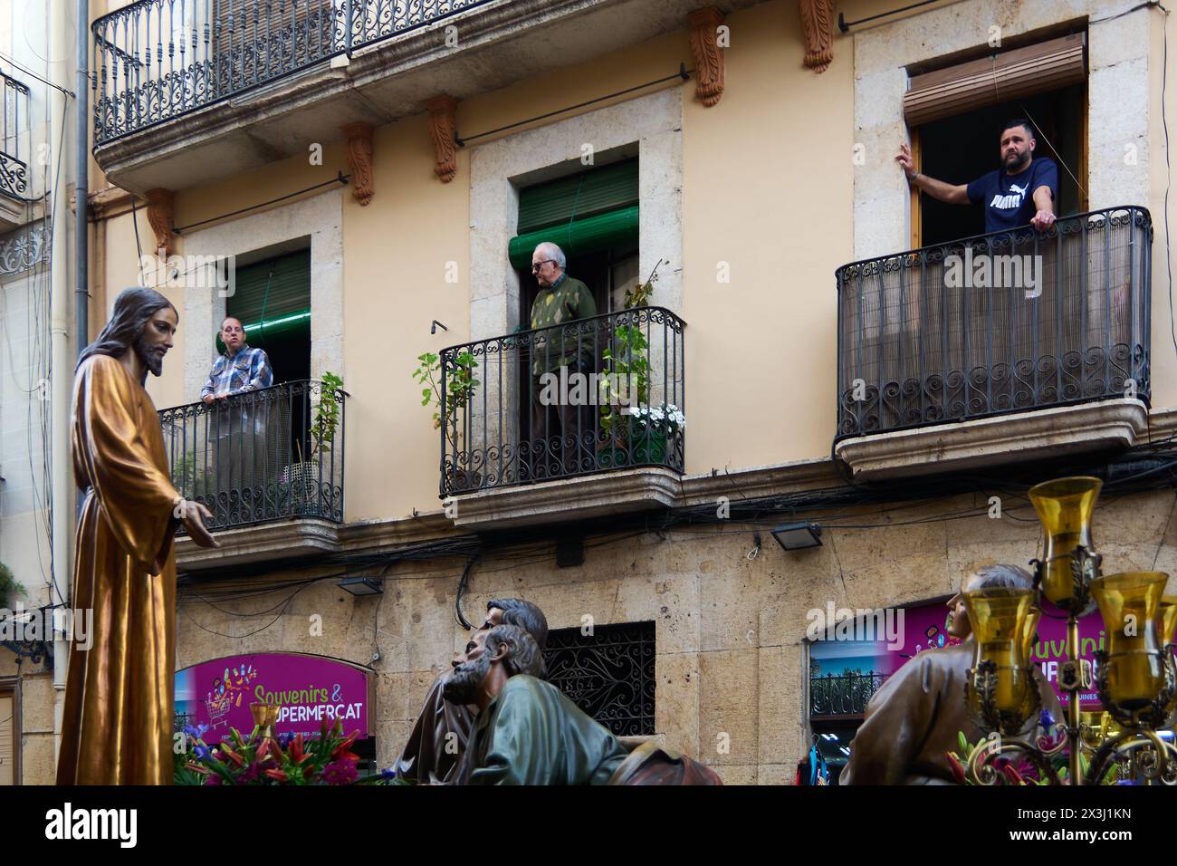 Tarragona, Spanien - 27. April 2024: Bild zeigt eine Karwochenprozession mit religiösen Statuen und Zuschauern, die von Balkonen in einem spanischen urb aus zusehen Stockfoto