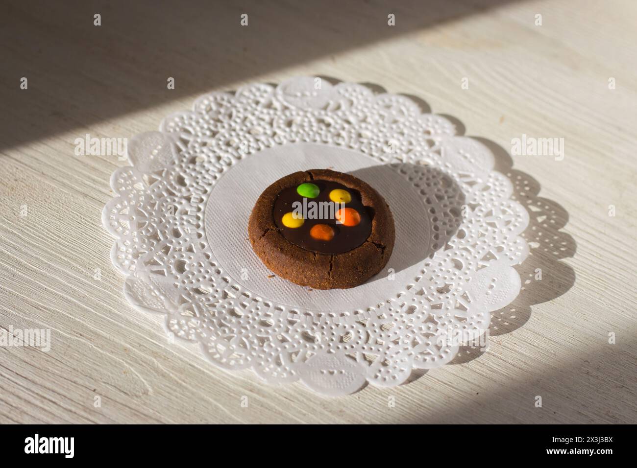 Runder Keks mit bunten Schokoladentropfen auf weißer Retro-Serviette. Süßes Dessert isoliert. Schokoladenkekse im Sonnenschein mit Schatten. Süße Bäckerei. Stockfoto
