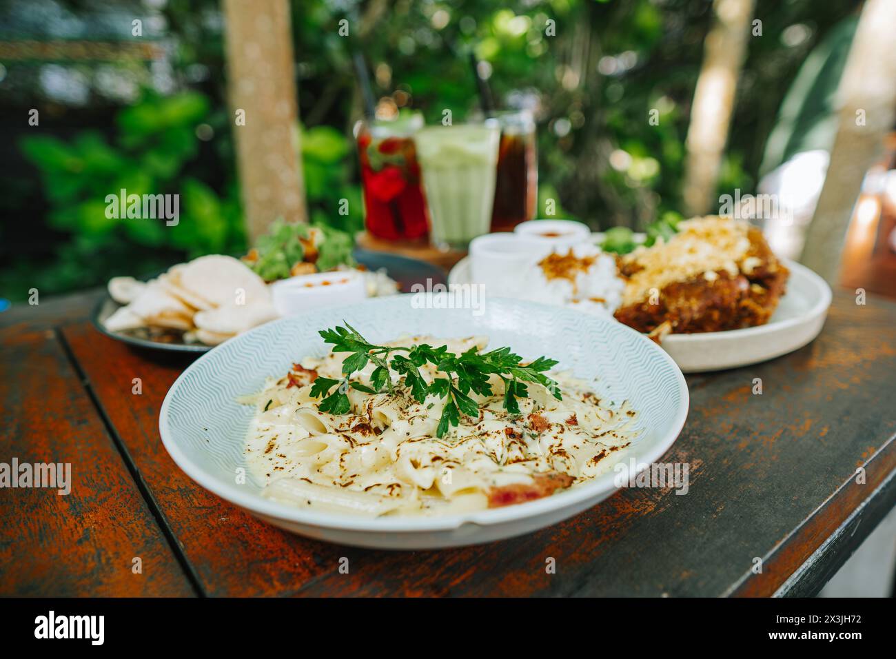 Indonesisch: Westliche Gerichte auf einem Holztisch zum Mittagessen. Konzentrierte sich auf Pasta mit verschwommenem, frittiertem Entenreis, gebratenem Reis und Cocktails Stockfoto