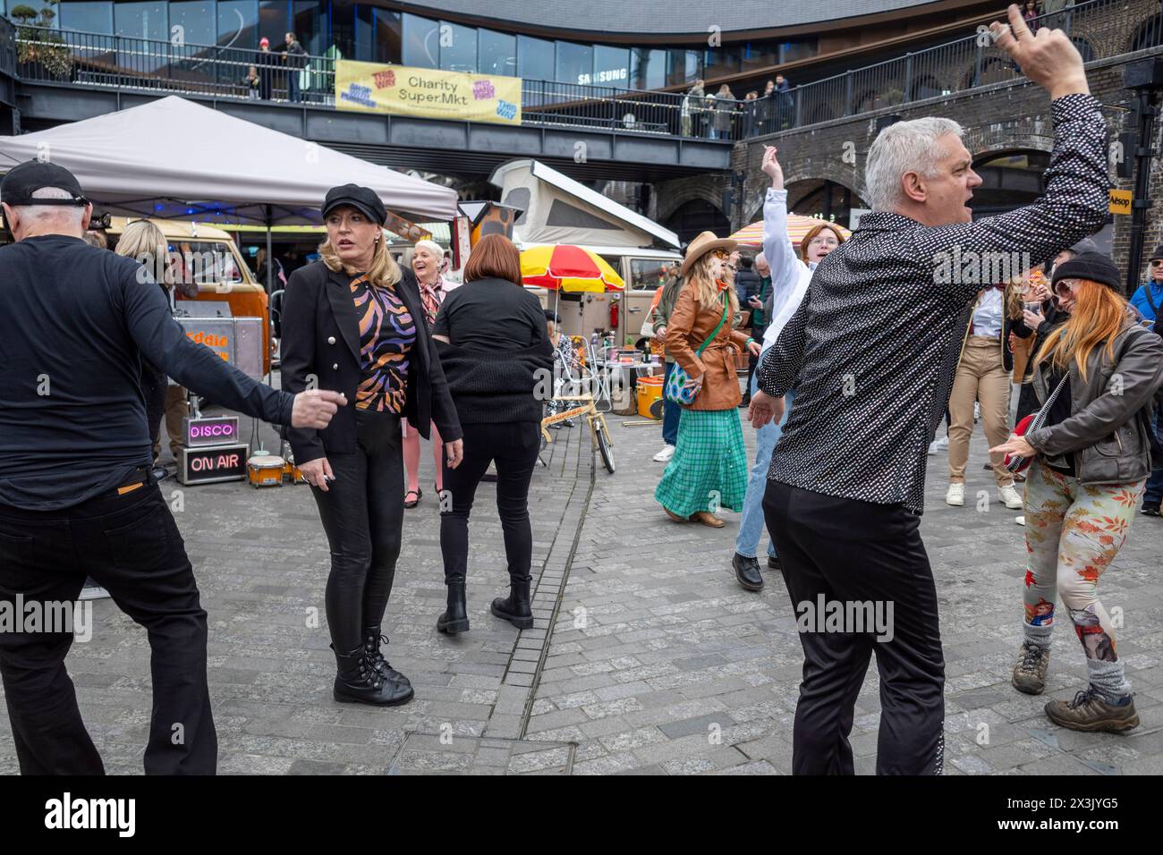 London, Großbritannien. 27. April 2024. Die Leute tanzen zur Musik der 60er und 70er Jahre, gespielt von DJ Eddie Lovebus beim Classic Car Boot Sale am Granary Square, King’s Cross. Die Veranstaltung feiert alles Vintage, von Mode und Schmuck bis hin zu Haushaltswaren und Schallplatten vor dem Hintergrund von Oldtimern. Quelle: Stephen Chung / Alamy Live News Stockfoto