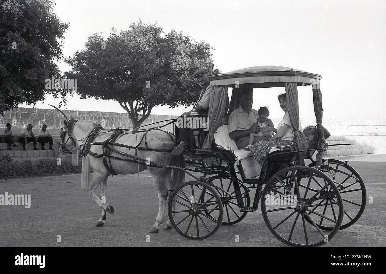 1960er Jahre, historisch, ein reifes Paar mit ihrem Enkel, der in einer Pferdekutsche sitzt, Nr. 49 auf der Seitenlampe, Malta. Die als Karrozzin bekannten Pferde und Kutschen als Transportmittel reichen bis in die 1850er Jahre zurück Stockfoto