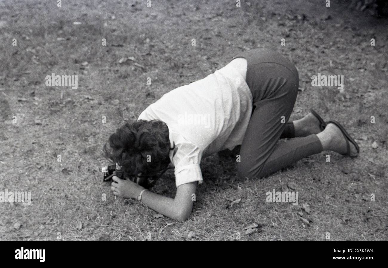 1960er Jahre, historisch, eine Frau in Bluse und Hosen, in krabbelnder Position mit Ellbogen und Knien auf dem Boden, ein Foto tief unten mit einer faltbaren Filmkamera der Epoche. Stockfoto