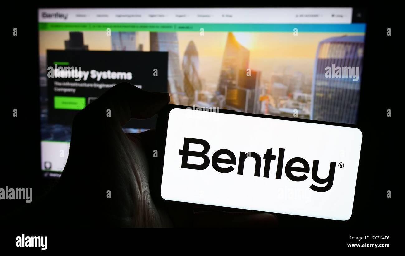 Person, die ein Mobiltelefon mit dem Logo des amerikanischen Softwareunternehmens Bentley Systems Inc. Vor der Webseite des Unternehmens hält. Schwerpunkt auf dem Display des Telefons. Stockfoto